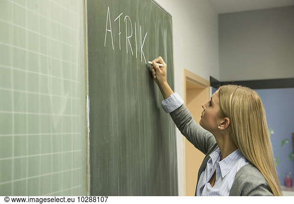 School teacher writing on blackboard in classroom  Munich  Bavaria  Germany