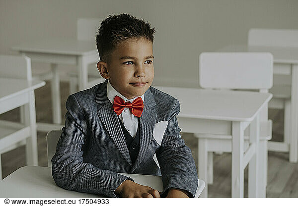 Schoolboy wearing red bow tie with suit sitting in classroom