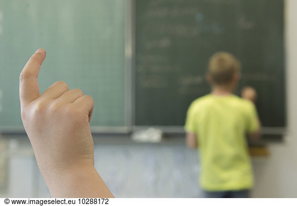 Schoolboy writing on blackboard and a schoolgirl raising hand in classroom  Munich  Bavaria  Germany