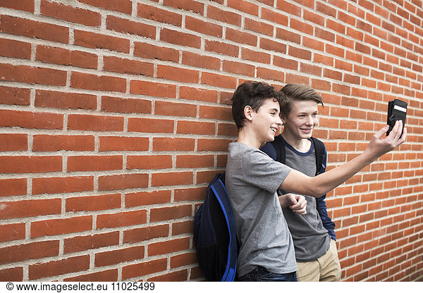 Schoolboys (12-13) taking selfie with mobile phone in front of building