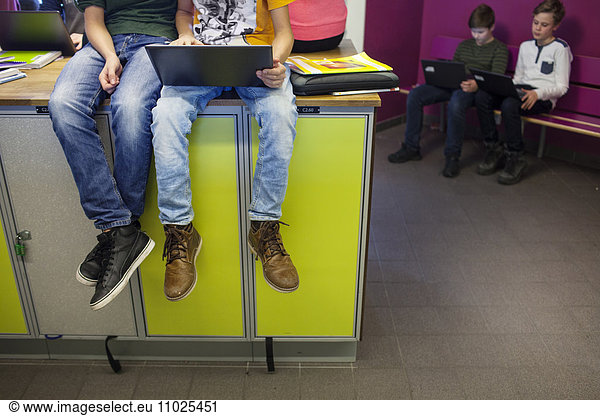 Schoolboys (12-13) using laptops in school corridor