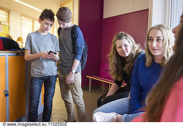 Schoolchildren (12-13) talking and using mobile phone in corridor
