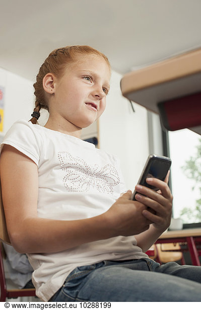 Schoolgirl holding a smart phone in classroom  Munich  Bavaria  Germany