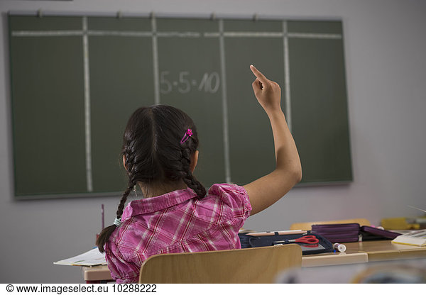Schoolgirl in front of blackboard with raised hand in classroom  Munich  Bavaria  Germany