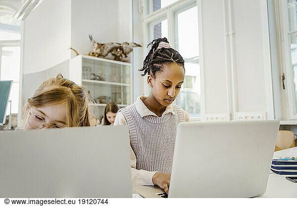 Schoolgirl using laptop sitting at desk in classroom