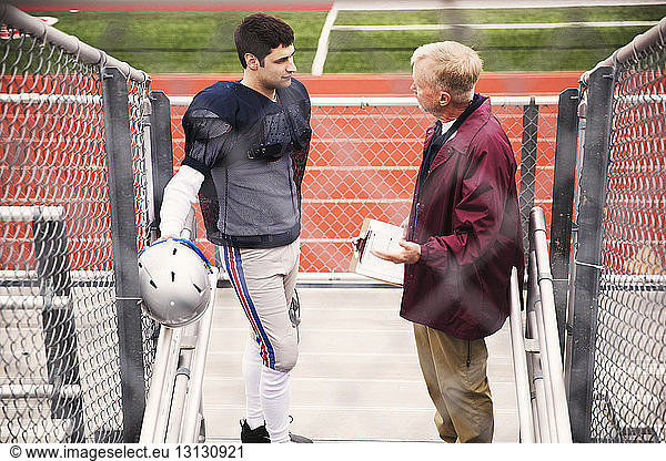 Schrägansicht des Trainers beim Gespräch mit einem American-Football-Spieler im Stadion