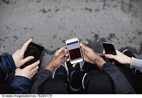 Schrägansicht von Freunden  die soziale Medien in Mobiltelefonen auf der Straße nutzen