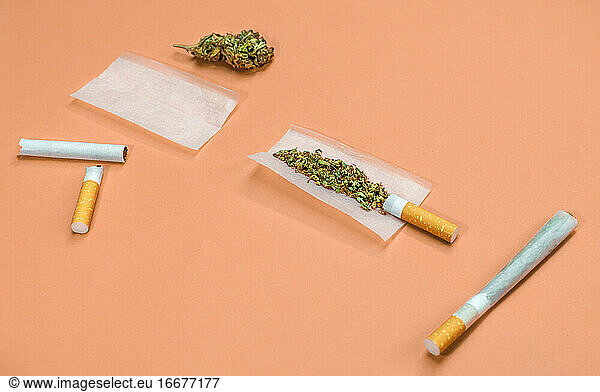 Schritte und Materialien zum Drehen eines Marihuana-Joints auf orangefarbenem Hintergrund.