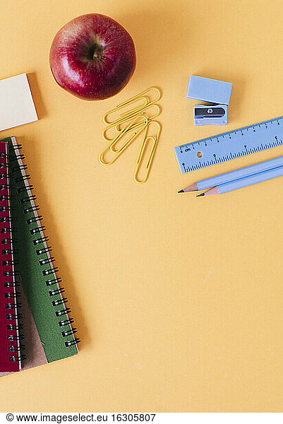 Schulsachen mit frischem Apfel auf gelbem Tisch