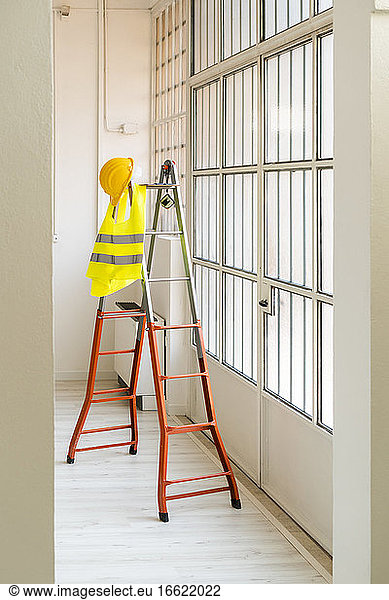 Schutzhelm und reflektierende Weste hängen an einer Leiter in einem leeren Studio