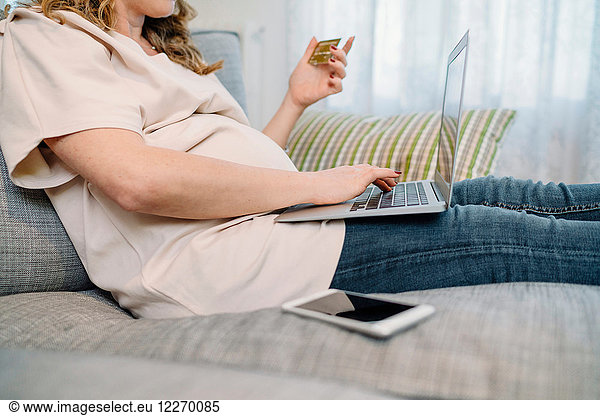 Schwangere Frau auf dem Sofa  die mit dem Laptop online einkauft  beschnitten