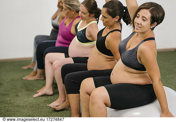 Schwangere Frau mit erhobener Hand auf Fitnessball sitzend