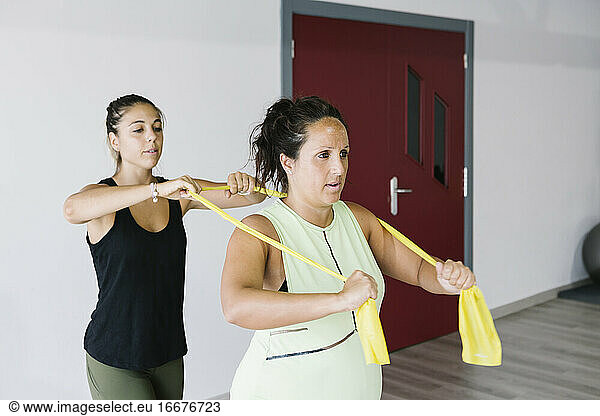 Schwangere Frau trainiert mit Gummibändern mit ihrem Personal Trainer