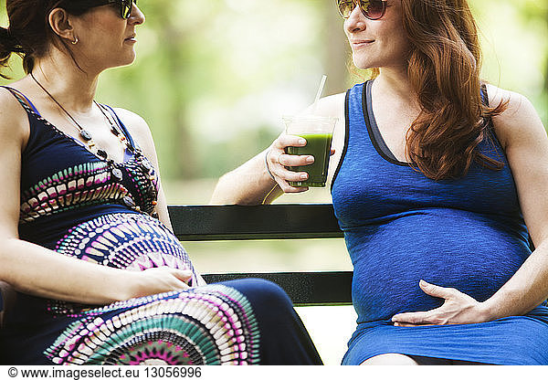 Schwangere Frauen im Gespräch auf einer Parkbank sitzend