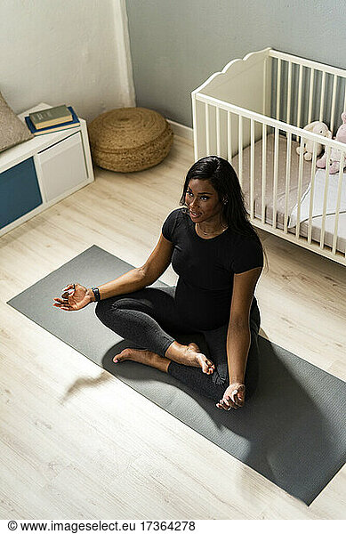 Schwangere junge Frau meditiert zu Hause auf einer Matte sitzend