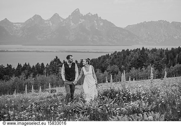 schwarz-weißes  glücklich lächelndes Brautpaar im Feld mit Wildblumen