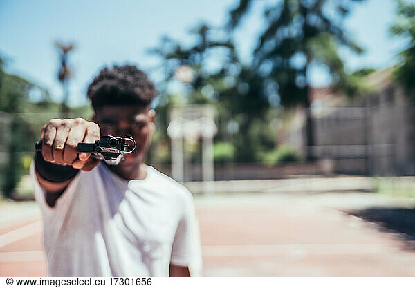 Schwarzer afroamerikanischer Junge auf einem Basketballplatz  der mit einer Waffe auf die Kamera zielt. Fokus auf die Waffe.