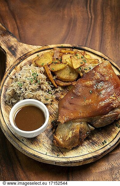 SCHWEINSHAXE traditionelle deutsche Schweinshaxe mit Sauerkraut und Kartoffeln bayerische Mahlzeit auf rustikalem Holz Hintergrund.