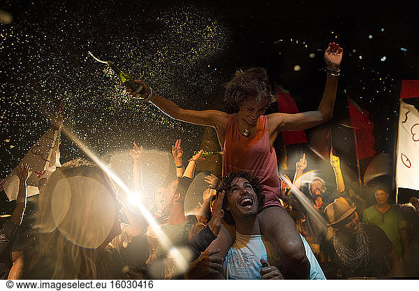 Schwelgt bei einem Open-Air-Konzert  lächelnder Mann trägt Frau auf den Schultern  Arme ausgestreckt  Bierflasche in der Hand.