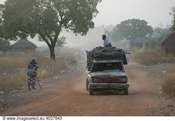 Schwer beladenes Auto auf der Dorfstraße im morgendlichen Dunst Houssere Faourou Kamerun Afrika