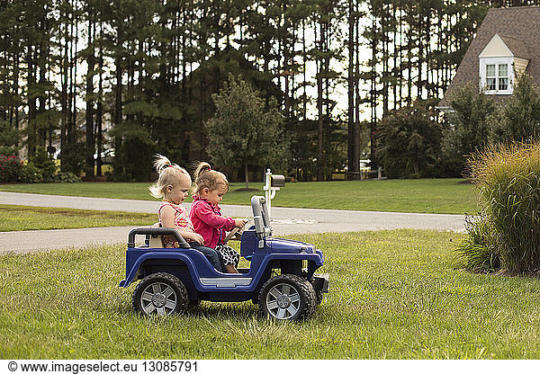 Schwestern fahren Spielzeugauto auf Grasfeld im Hinterhof