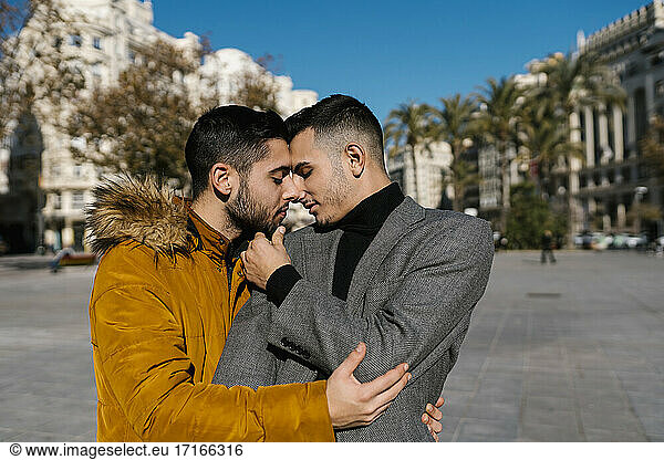 Schwule Männer mit Jacke stehen sich mit geschlossenen Augen in der Stadt gegenüber