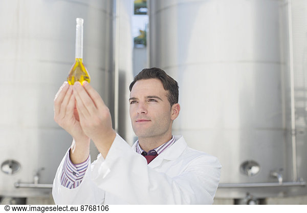 Scientist examining liquid in beaker next to silage storage towers