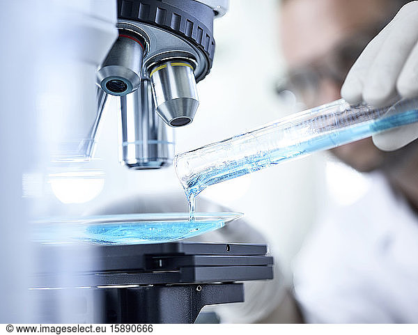 Scientist pouring blue liquid in bowl under microscope