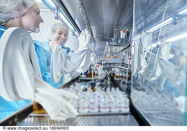 Scientist wearing protective glove giving high-five in microbiological safety cabinet