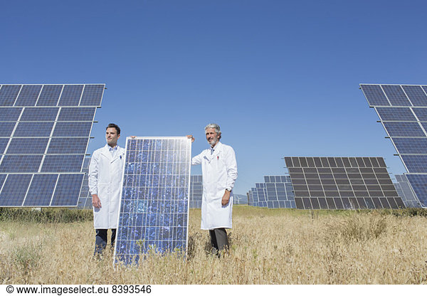 Scientists holding solar panel in rural landscape