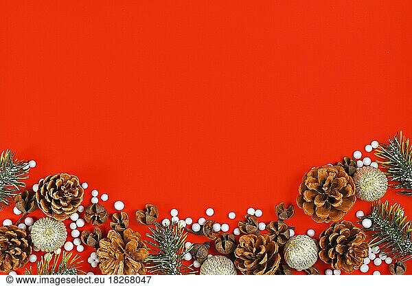 Seasonal Christmas flat lay with snow covered pine tree branches  tree bauble ornaments  pine cones and white balls at bottom of red background with empty copy space