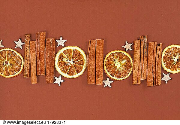 Seasonal natural dried orange slices  cinnamon sticks and star ornaments in a row on brown background