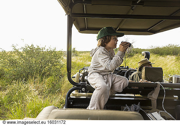 Sechsjähriger Junge mit Fernglas im Safari-Fahrzeug  Botswana