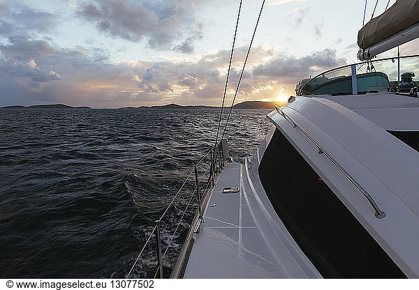 Segelboot fährt bei Sonnenuntergang auf See gegen bewölkten Himmel