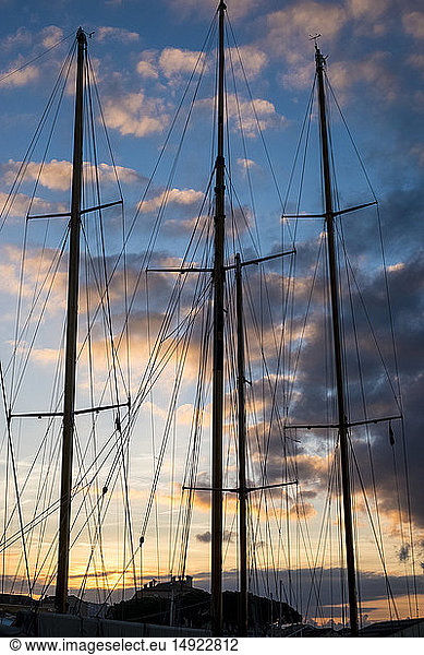 Segelschiffmasten und Takelage gegen einen bewölkten Himmel bei Sonnenuntergang.