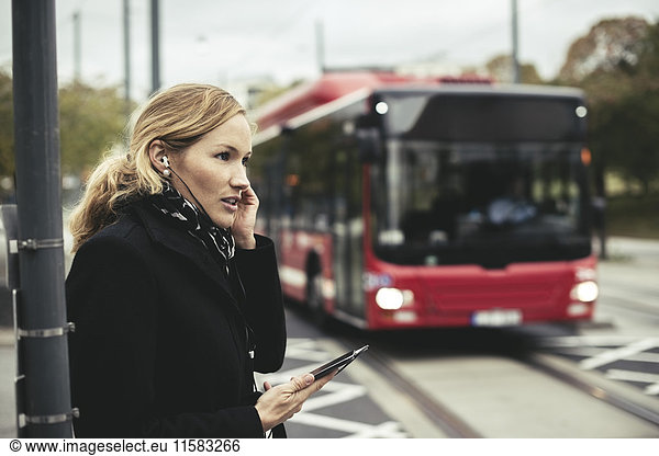 Seitenansicht der Geschäftsfrau im Gespräch auf dem Handy mit Bus im Hintergrund
