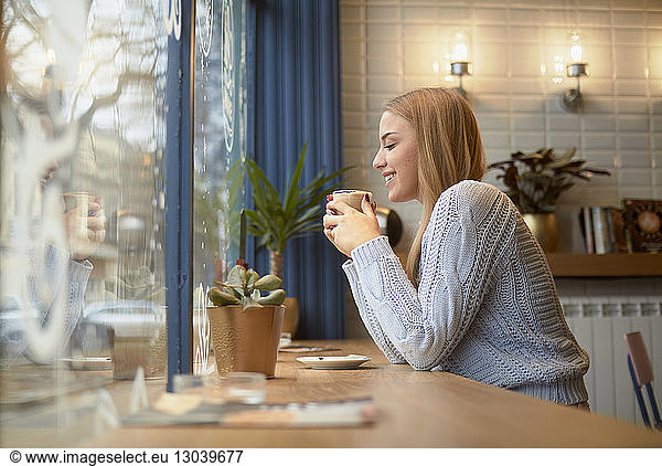 Seitenansicht einer Frau bei einem Drink am Tisch in einem Café