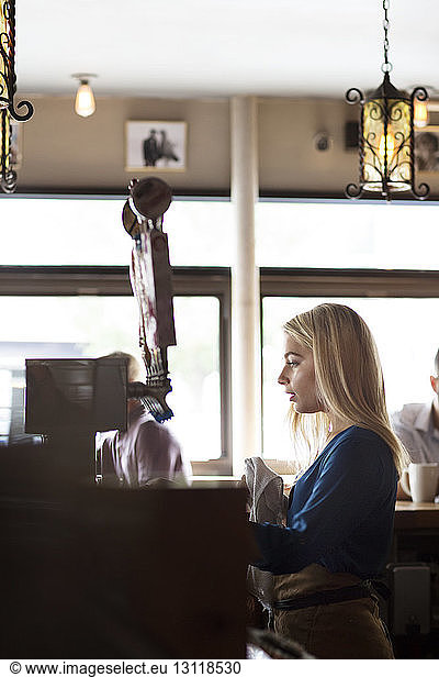 Seitenansicht einer Frau  die von Kunden im Cafe an der Theke steht