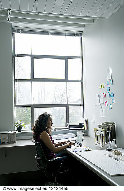 Seitenansicht einer Geschäftsfrau mit Laptop-Computer am Schreibtisch im Büro