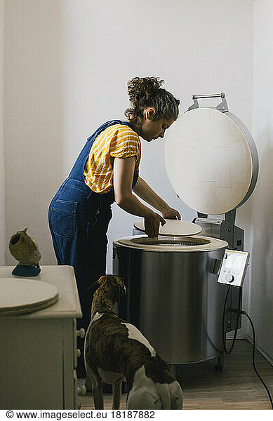 Seitenansicht einer Handwerkerin  die bei ihrer Arbeit zu Hause eine Keramikplatte in einen elektrischen Brennofen legt