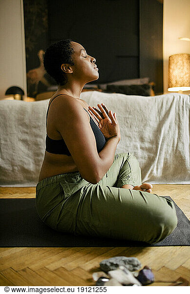 Seitenansicht einer jungen Frau beim Meditieren im Schlafzimmer zu Hause