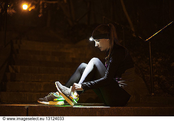 Seitenansicht einer jungen Frau mit beleuchtetem Scheinwerfer  der die Schnürsenkel auf den Stufen bindet
