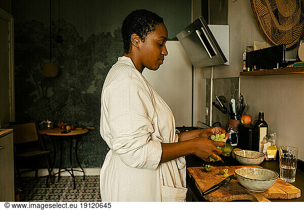 Seitenansicht einer jungen Frau mit Weintrauben am Küchentisch