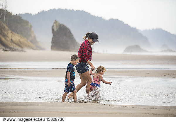 Seitenansicht einer Mutter  die mit ihren zwei kleinen Kindern am Strand spazieren geht.