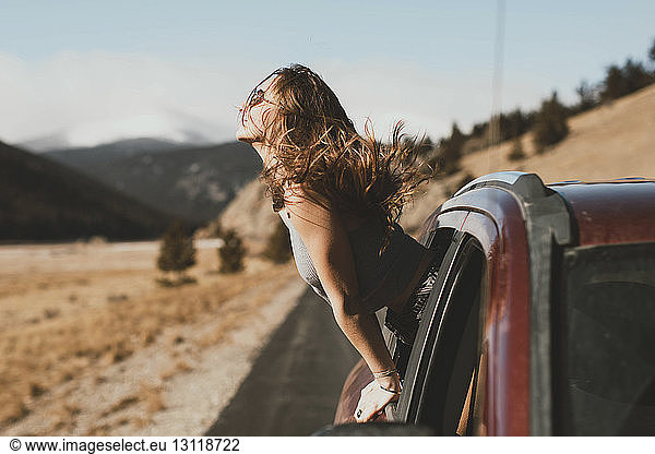 Seitenansicht einer sorglosen jungen Frau mit zerzaustem Haar  die sich aus dem Autofenster lehnt