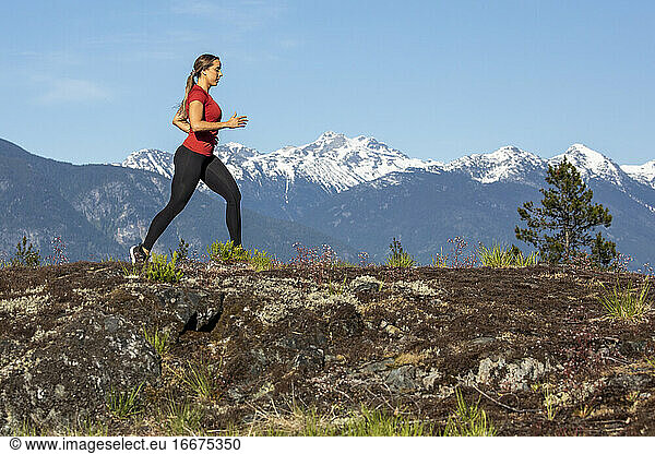 Seitenansicht einer starken Sportlerin  die beim Fitnesstraining auf dem Lande gegen einen verschneiten Bergrücken läuft