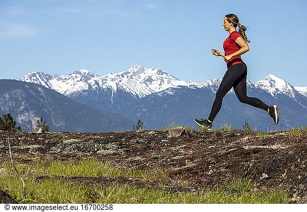 Seitenansicht einer starken Sportlerin  die beim Fitnesstraining auf dem Lande gegen einen verschneiten Bergrücken läuft