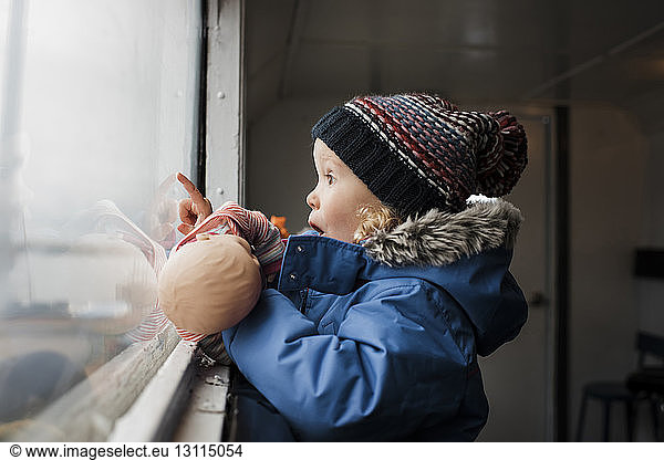 Seitenansicht eines überraschten Mädchens mit Spielzeug  das durch ein Fenster schaut