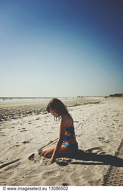 Seitenansicht eines Mädchens  das am Strand von St. Augustine Beach vor klarem Himmel bei strahlendem Sonnenschein auf Sand sitzt
