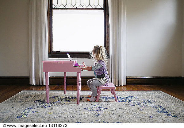 Seitenansicht eines Mädchens  das zu Hause am Fenster Spielzeugklavier spielt